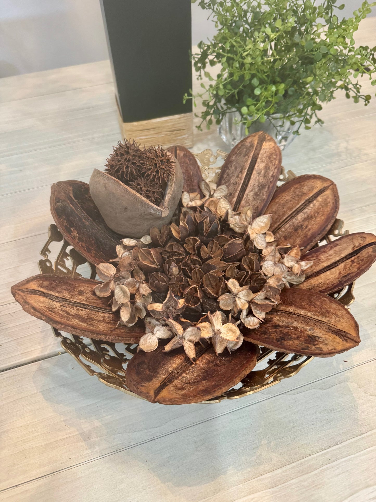 Decorative arrangement of dried plants in a metal bowl on a wooden surface.