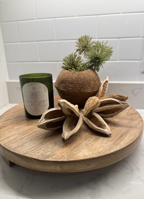 Decorative items including a candle, coconut with plants, and wooden flower on a round wooden tray.
