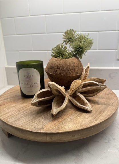 Decorative items including a candle, coconut with plants, and wooden flower on a round wooden tray.