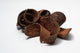 A photo of a pile of Elephant Ear Pods. They are brown texture seed pods on a white background.