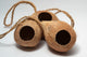 A photo of 3 Hanging Coconut Shell Hideout. They are brown textured shell hideouts on a white background.