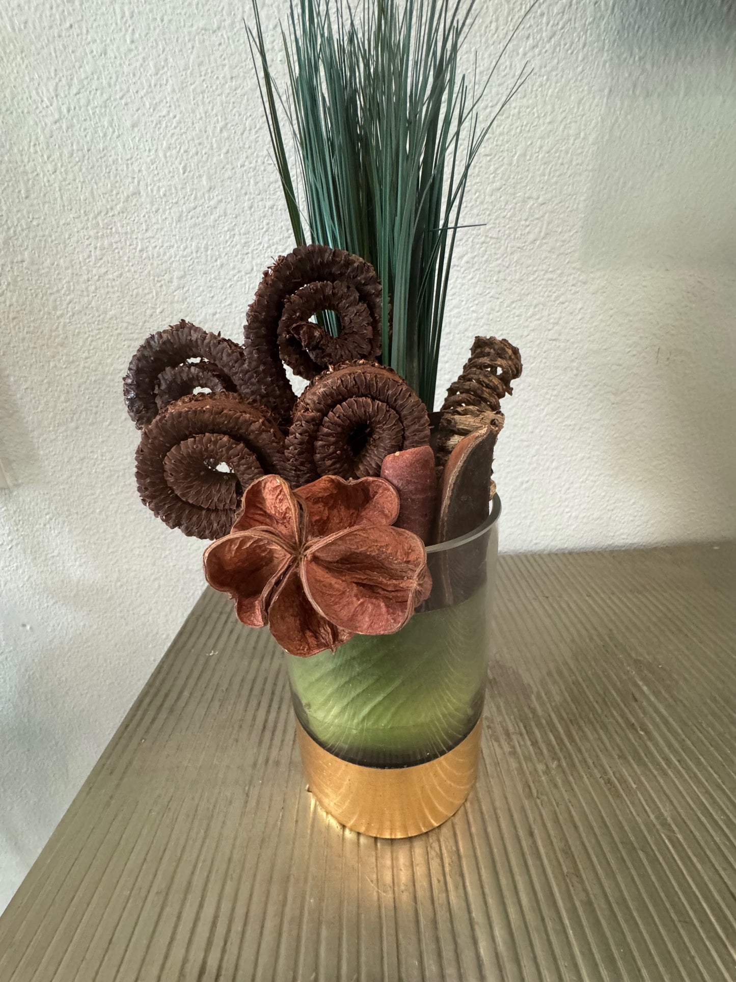 Decorative arrangement with brown flowers and greenery in a glass vase on a textured surface.