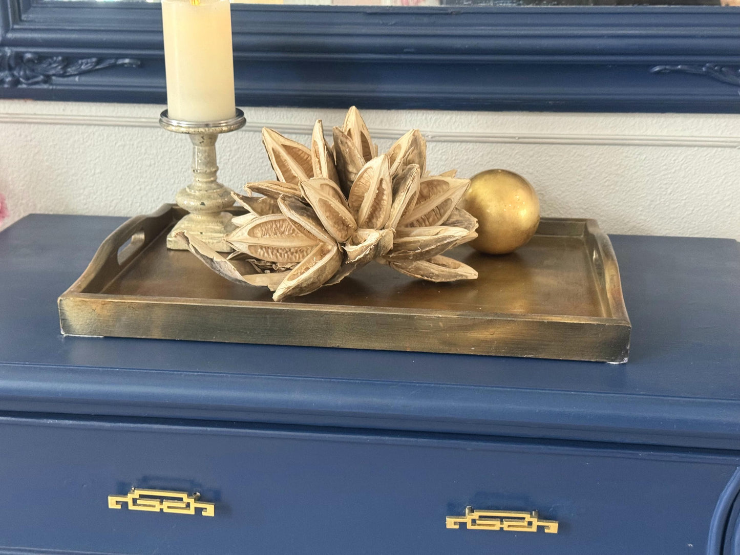 Decorative tray with a candle, floral arrangement, and sphere on a blue surface.