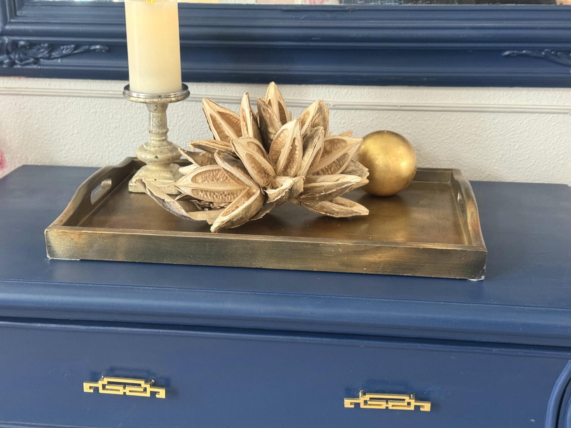 Decorative tray with a candle, floral arrangement, and sphere on a blue surface.