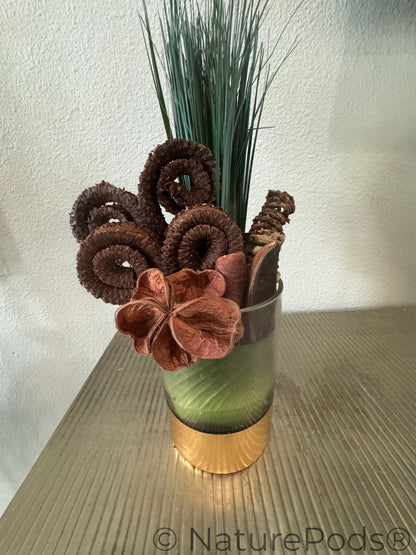 Decorative arrangement with brown flowers and greenery in a glass vase on a textured surface.